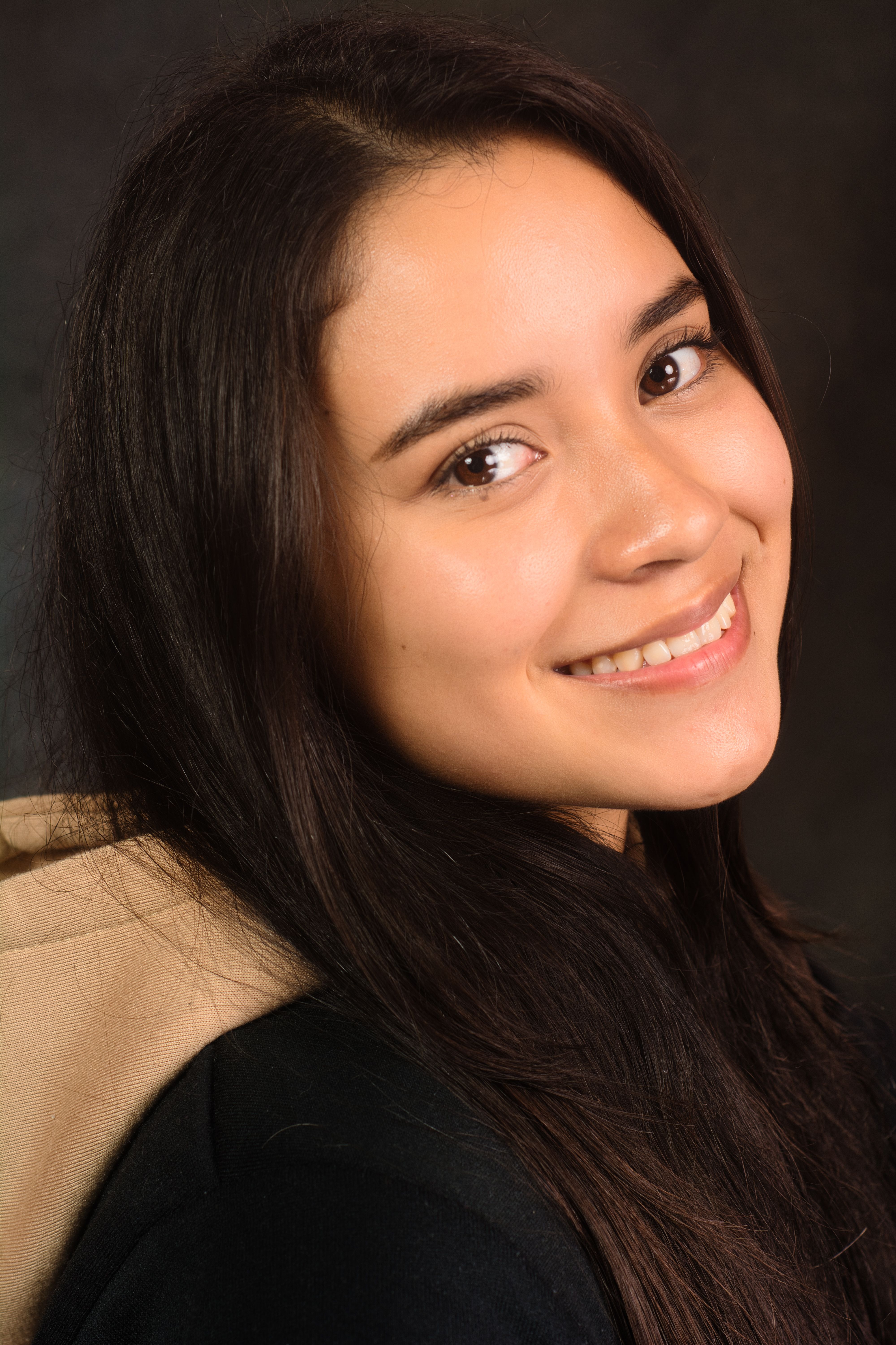 Close-up portrait of a smiling woman with long hair in casual attire against a dark background.