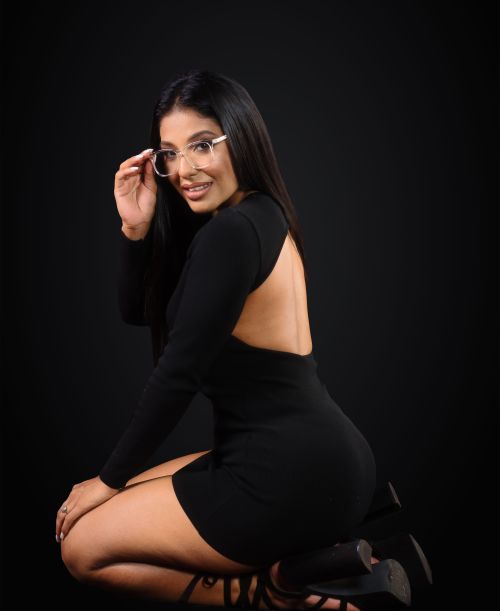 Free Stylish woman posing in a black dress with glasses, exuding elegance and confidence. Stock Photo