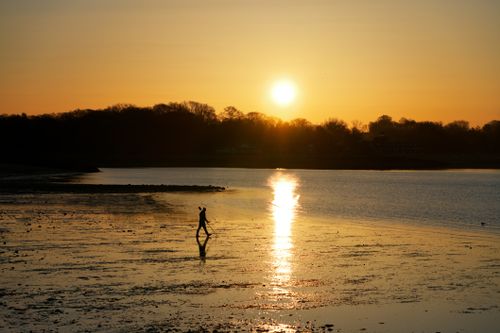 Free A serene silhouette of a person walking along the shore during a stunning sunset. Stock Photo