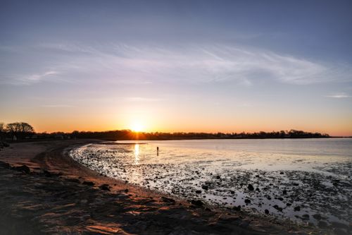 Free Serene sunset over a tranquil beach, highlighting the calm sea and a distant figure on the shoreline. Stock Photo