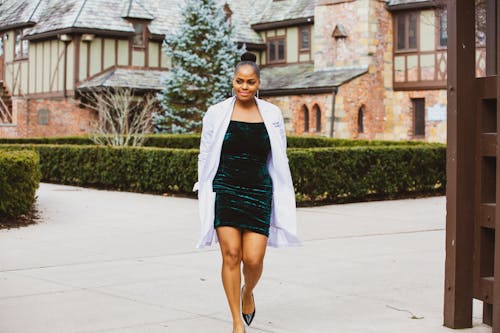 Woman in Green Dress and White Coat Walking on Gray Concrete Floor