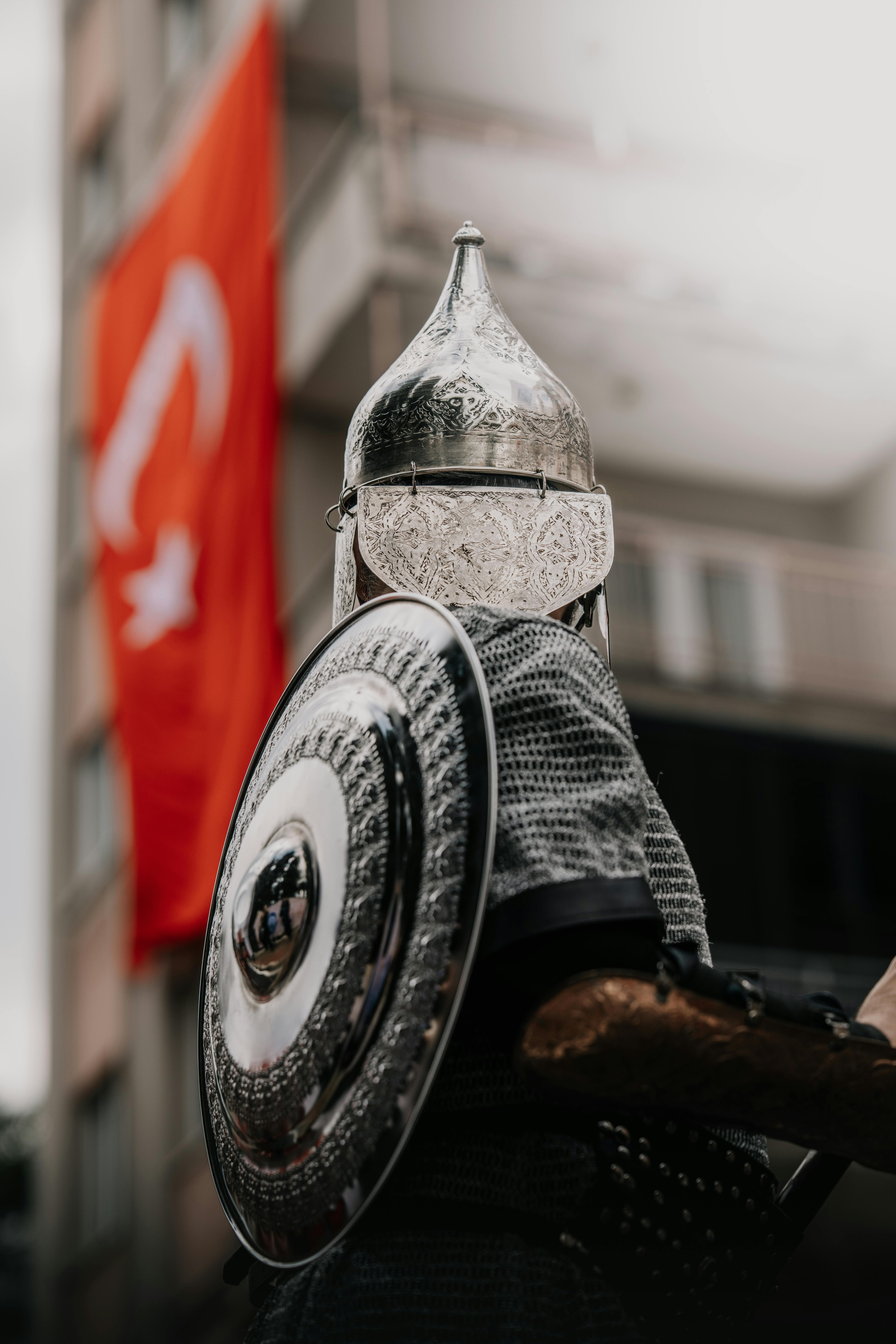 A historic Ottoman warrior in traditional attire posed by a Turkish flag in Bursa, Türkiye.