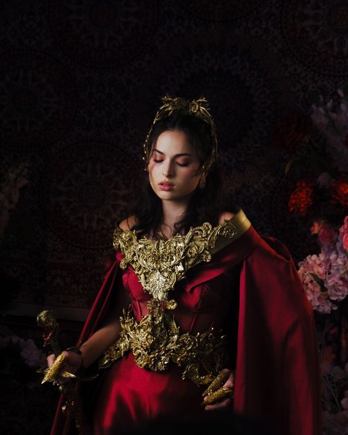 Free Beautiful woman in a luxurious red and gold medieval-inspired dress, posing indoors. Stock Photo