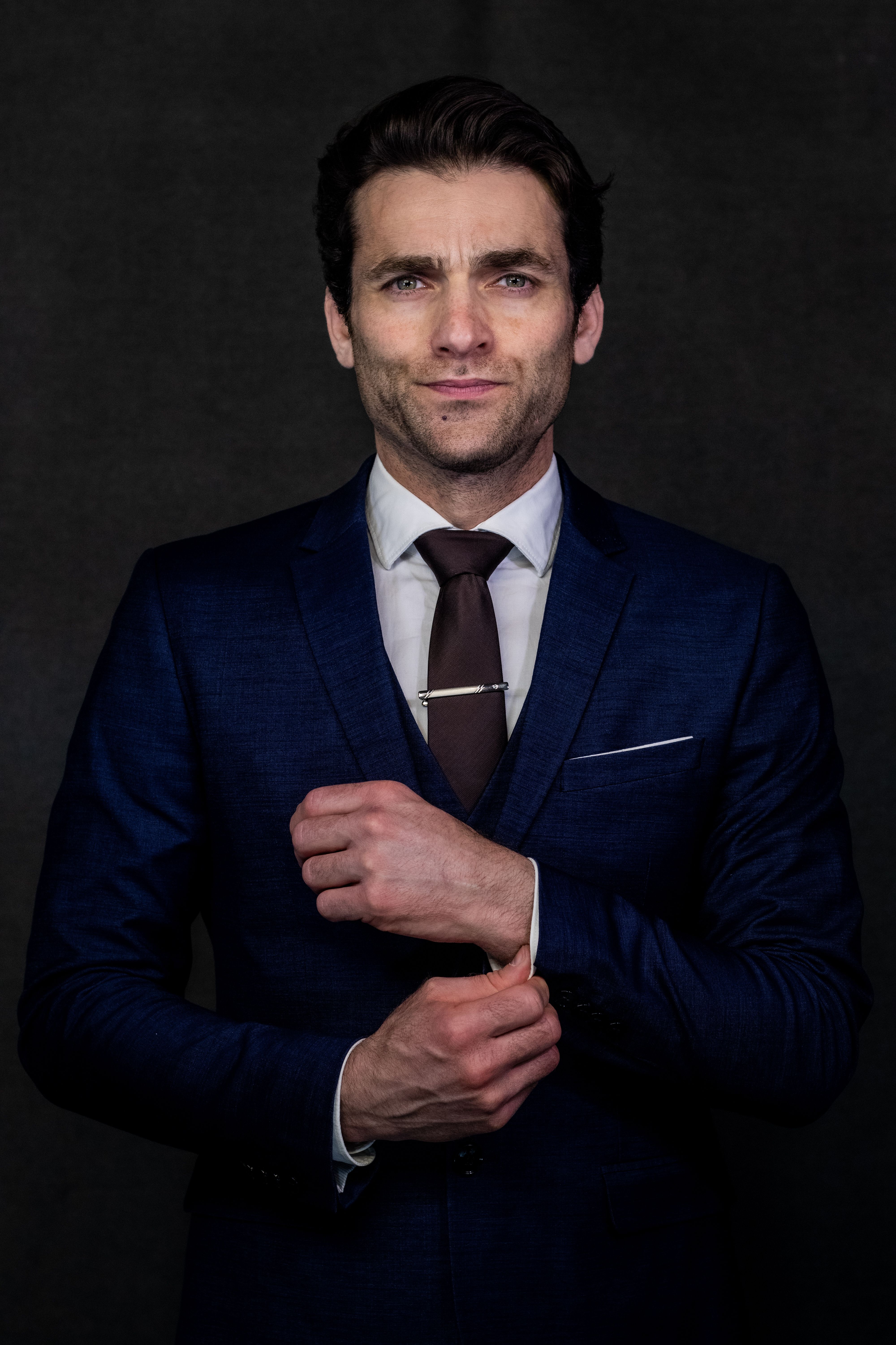 Portrait of a confident man in a blue suit, adjusting his cuffs.