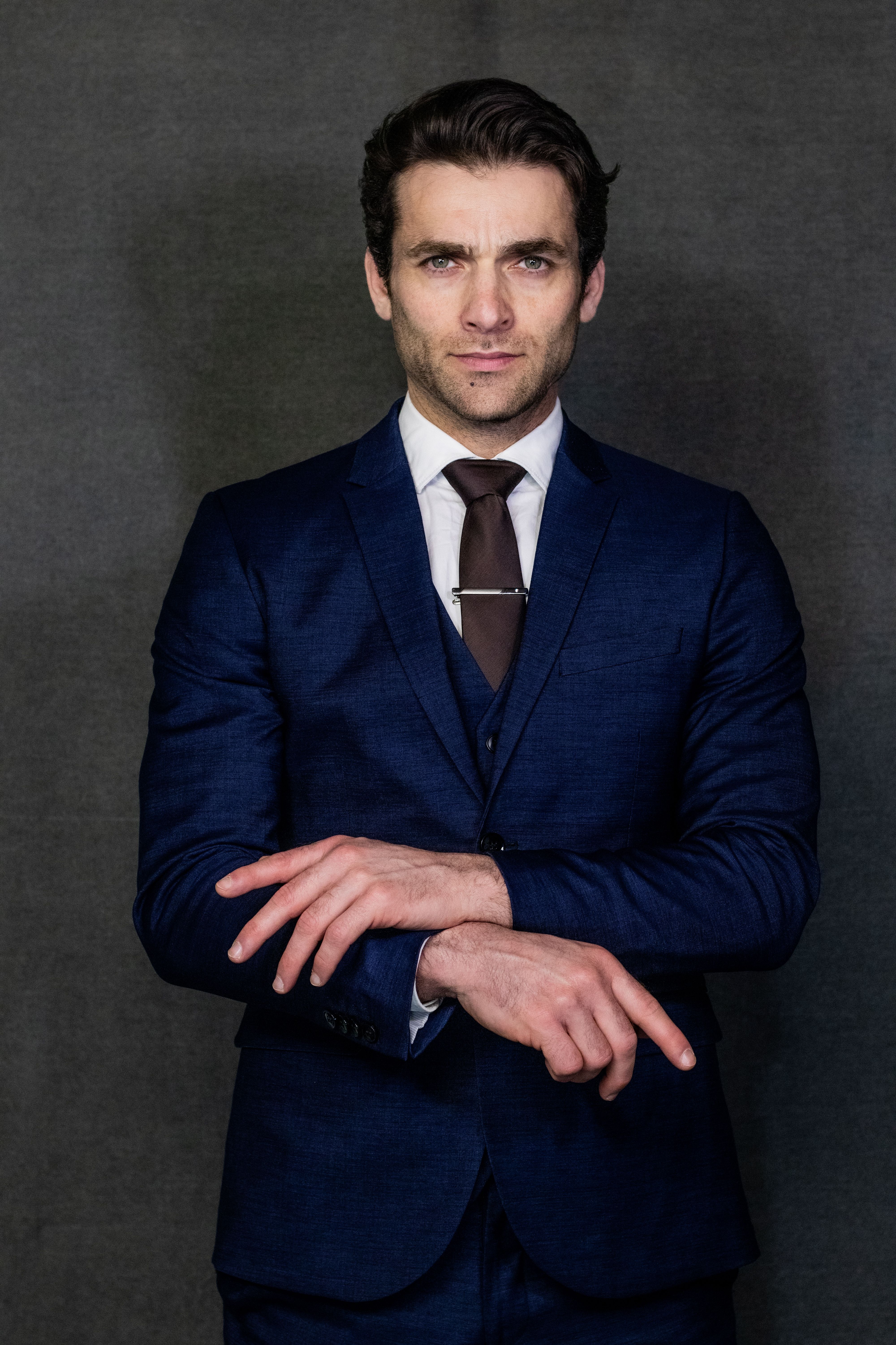 Professional adult man in blue suit posing confidently against gray background.