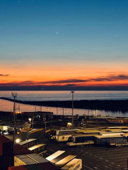 Captivating sunset over a bustling port with vibrant sky and sea horizon.