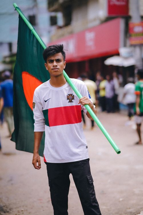 Free A young man stands confidently in an urban setting holding a Bangladesh national flag. Stock Photo