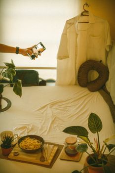 A cozy bedroom setup with a smartphone, plants, and a noodle dish creating a relaxed ambiance.