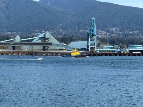 Tugboat navigating Vancouver Harbor near industrial port with mountain backdrop.