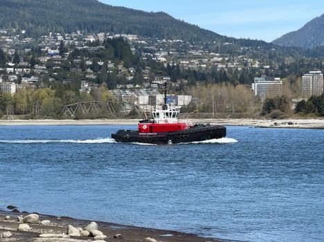 Red tugboat navigating coastal waters against mountain backdrop, near Vancouver.