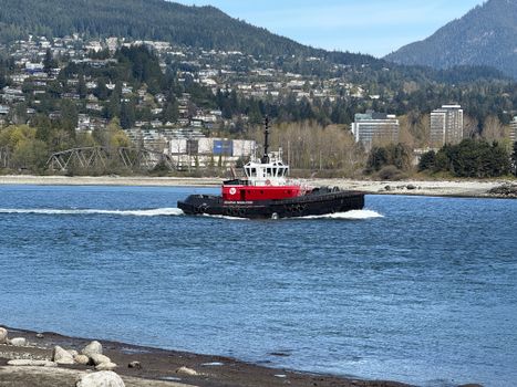 A vibrant tugboat sails along Vancouver's beautiful waterfront with city and mountain views.