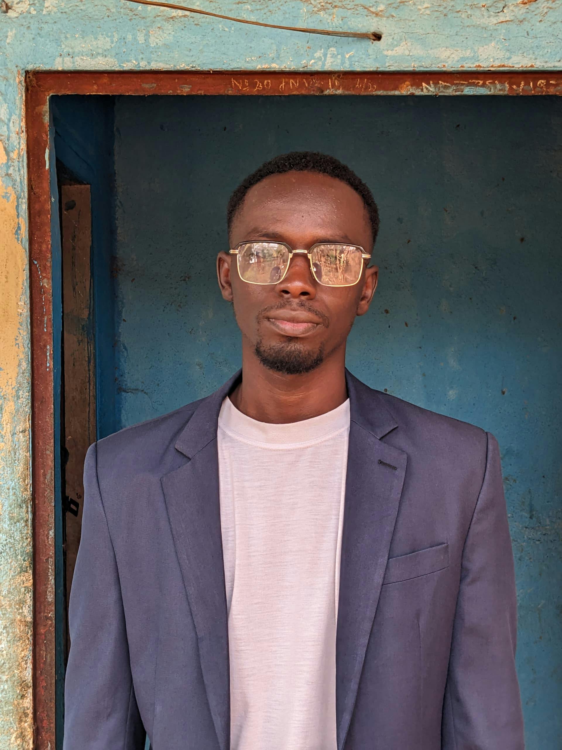 Portrait of a man in sunglasses and blazer against a textured wall, showcasing confidence.