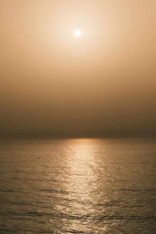 Free A beautiful sunset over the ocean casting a golden reflection on calm waves. Stock Photo