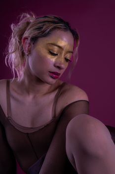 A striking portrait of a woman with golden face paint in moody lighting on a purple background.