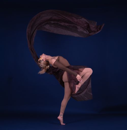 Free Captivating image of a dancer executing a stunning leap with flowing fabric against a blue backdrop. Stock Photo
