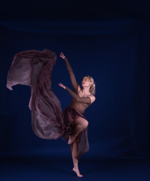 Free A ballet dancer poses elegantly with a flowing dress on a dark blue background. Stock Photo