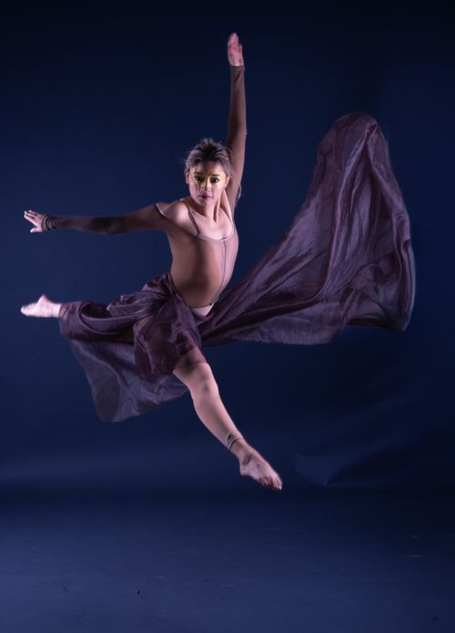 Free A dancer in mid-air performing a leap with a flowing skirt against a dark background. Stock Photo
