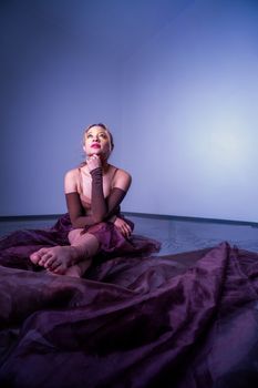 A woman in a dark dress posing thoughtfully on a draped floor, under ambient lighting.