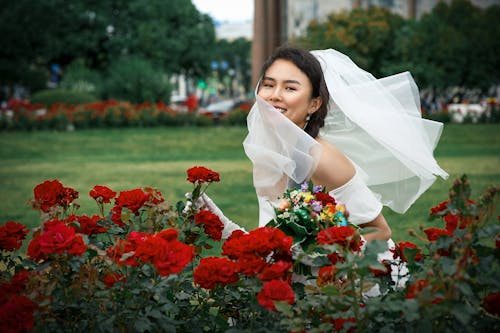 Woman in White Wedding Dress Holding Red Flowers