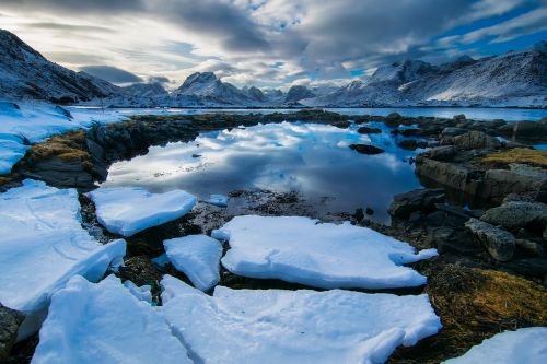 Free A breathtaking view of a snowy Arctic landscape with a serene lake reflecting the sky and mountains. Stock Photo