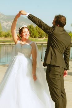 A happy bride and groom dance together outdoors on a bright sunny day.