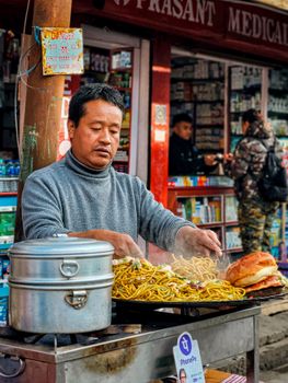Street vendor cooking noodles in bustling market setting in Darjeeling, West Bengal, India.