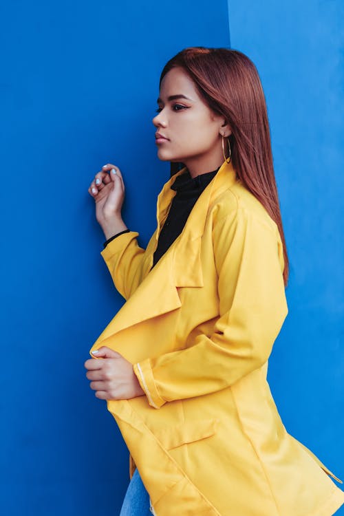 Free Woman in Yellow Coat Standing Near Blue Wall Stock Photo