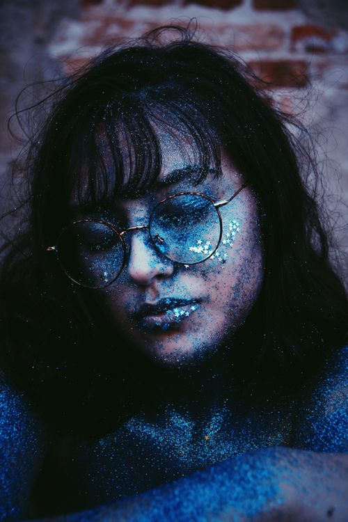 Free Close-up portrait of a young woman wearing sunglasses and covered in blue glitter for a fashion photoshoot. Stock Photo
