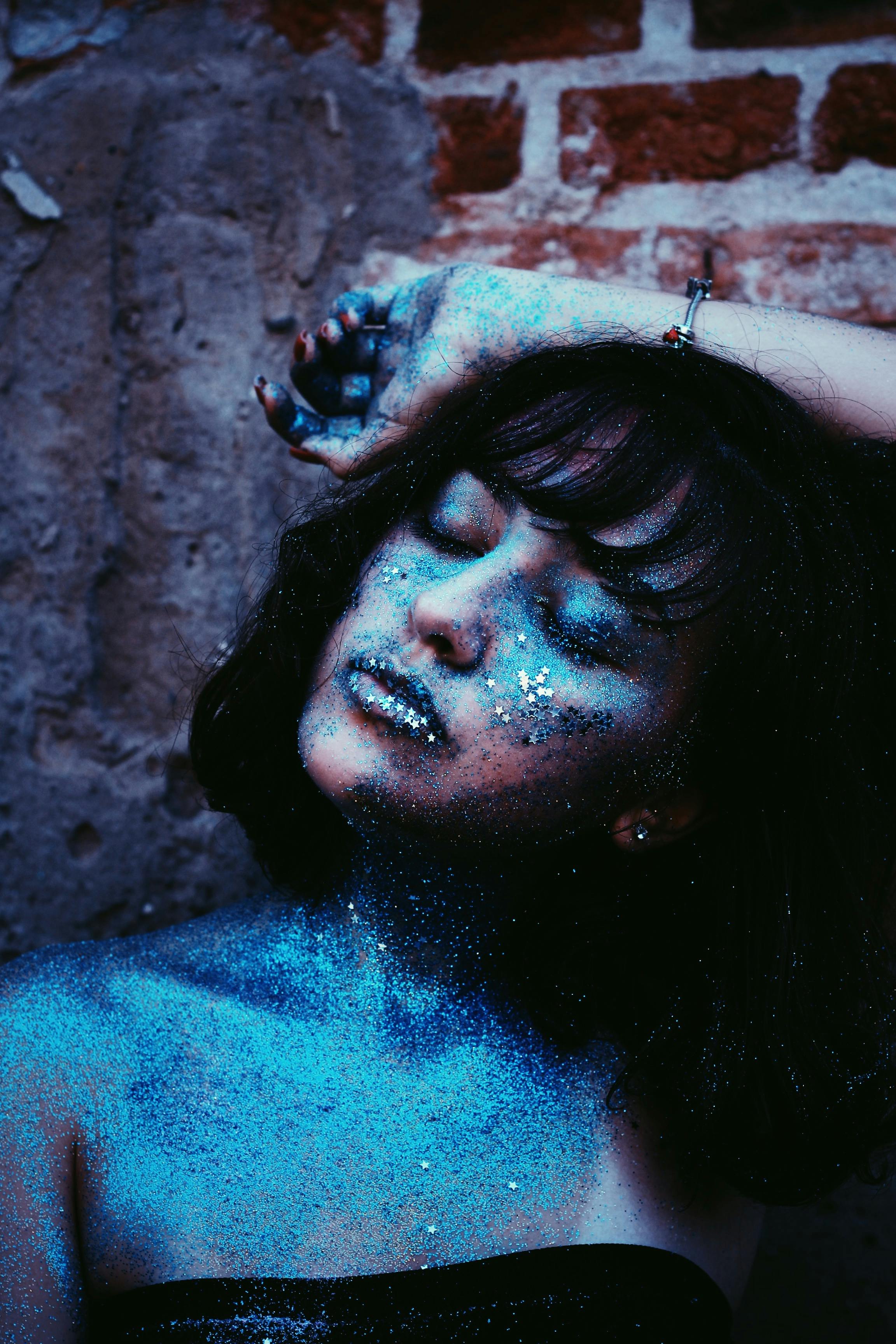 woman with blue glitters leaning on brown wall