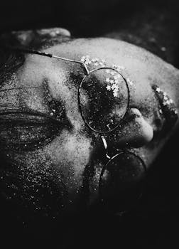 一张戴着闪光灯和眼镜的女人脸的黑白特写肖像，捕捉到艺术和梦幻的氛围