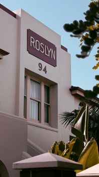 Close-up of building facade with Roslyn sign and number 94, surrounded by tropical plants.