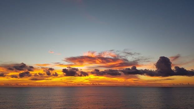 Captivating sunset with fiery orange clouds reflecting over the calm ocean waters.