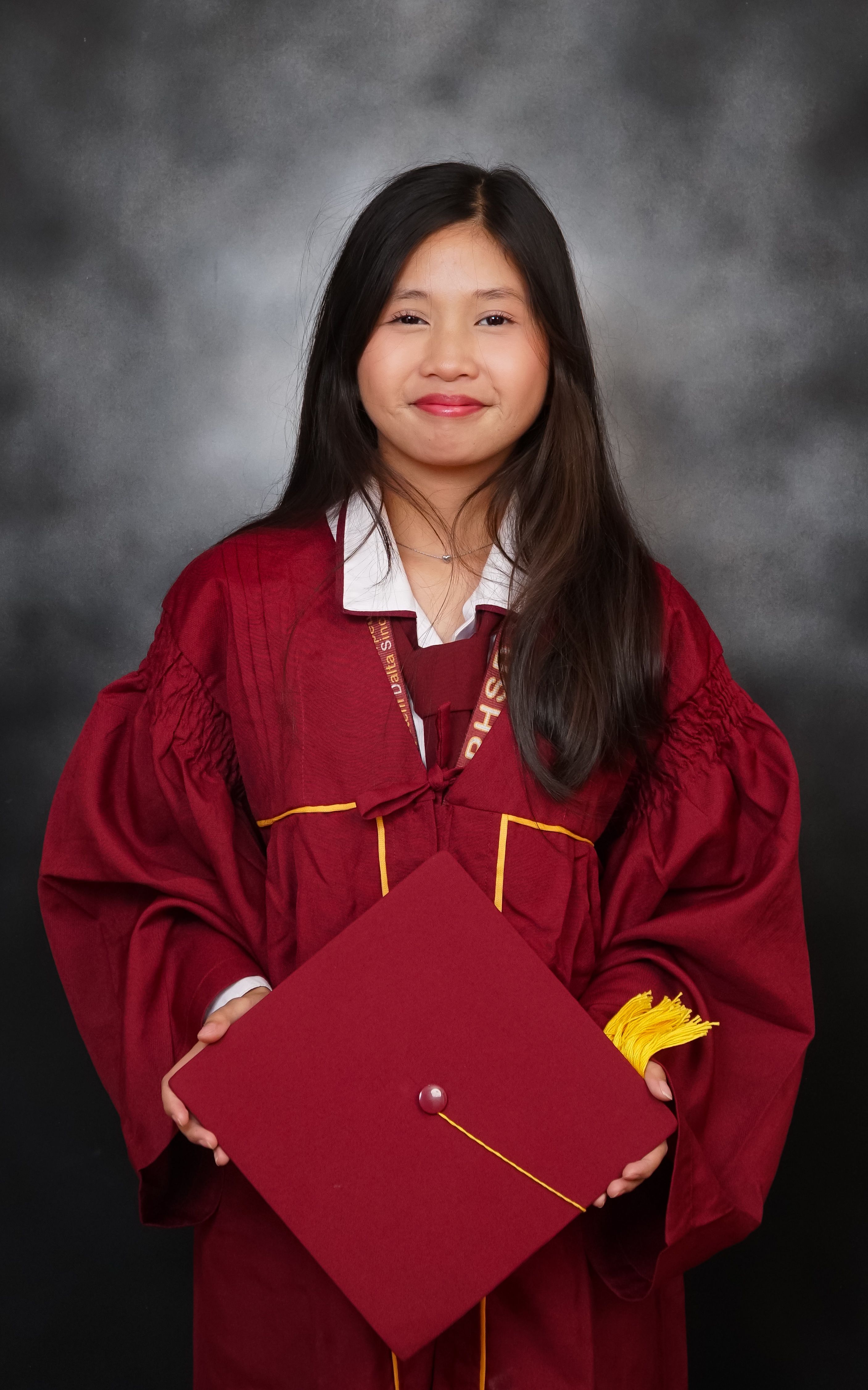 Portrait of a young graduate in maroon gown holding graduation cap, smiling.
