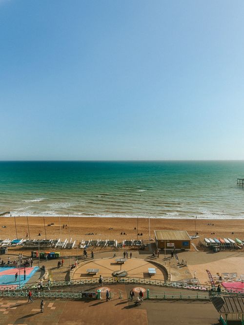 Free Aerial view of a bustling beach with vibrant blue sea under a clear sky, capturing summer leisure. Stock Photo