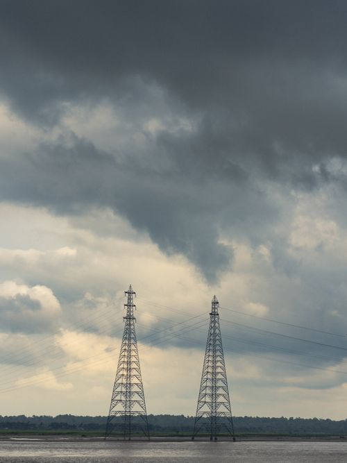 Free High voltage power lines stretch across a river under a stormy sky. Stock Photo
