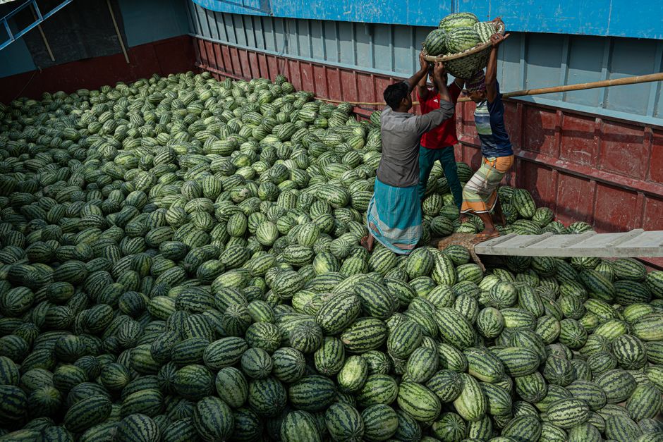 Photo by Galib Rahman Nadim Three workers load watermelons onto a ship, showcasing teamwork in agriculture.