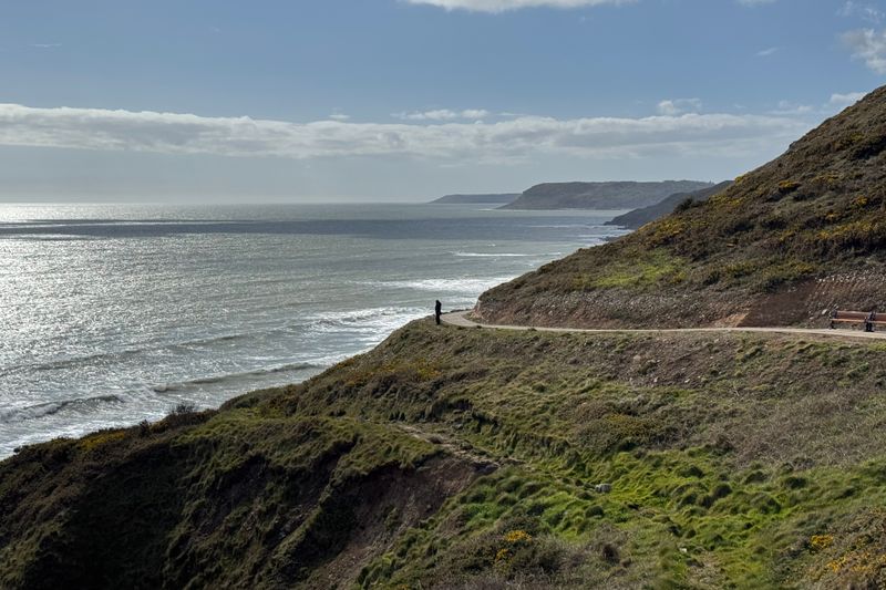 Breathtaking coastal cliffs of Wales with a lone figure admiring the ocean view.