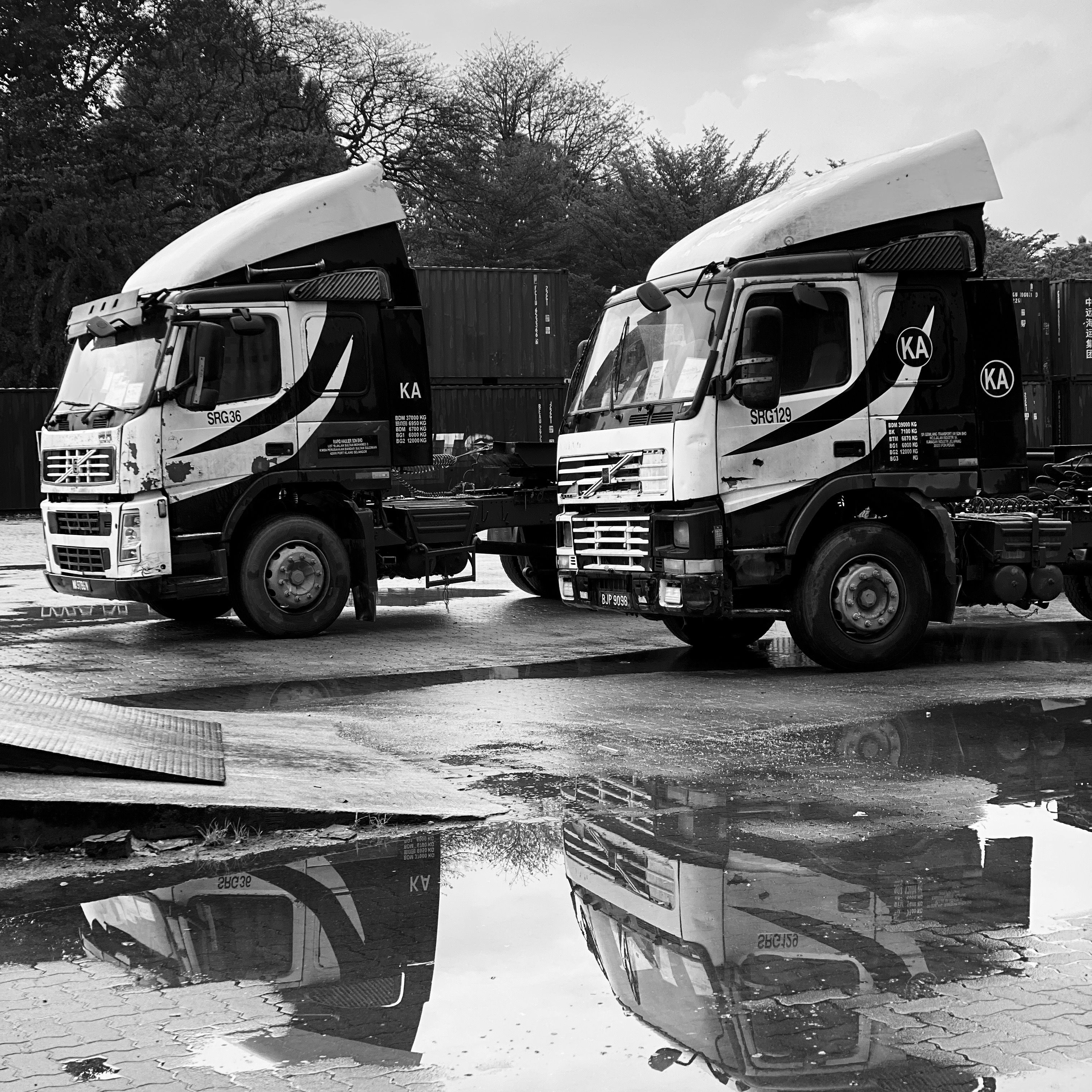 Monochrome image of industrial trucks reflecting in a puddle, showcasing transportation and logistics.