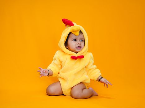 Cute baby wearing a chicken costume sitting against a bright orange background, perfect for festive or playful themes.