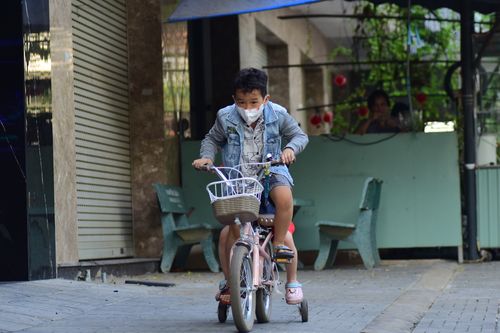 Free Young boy wearing a mask rides a bicycle with training wheels on an urban street. Stock Photo