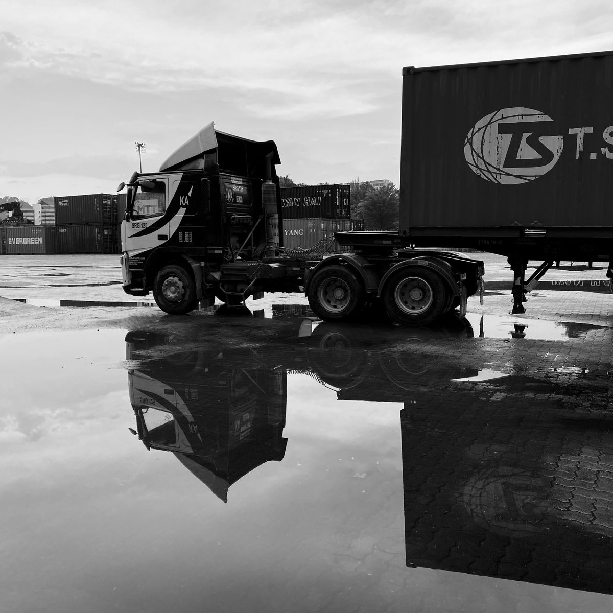 Prime mover and container in a transport yard after rain — the large panel area that drives the cost of a lorry sticker job
