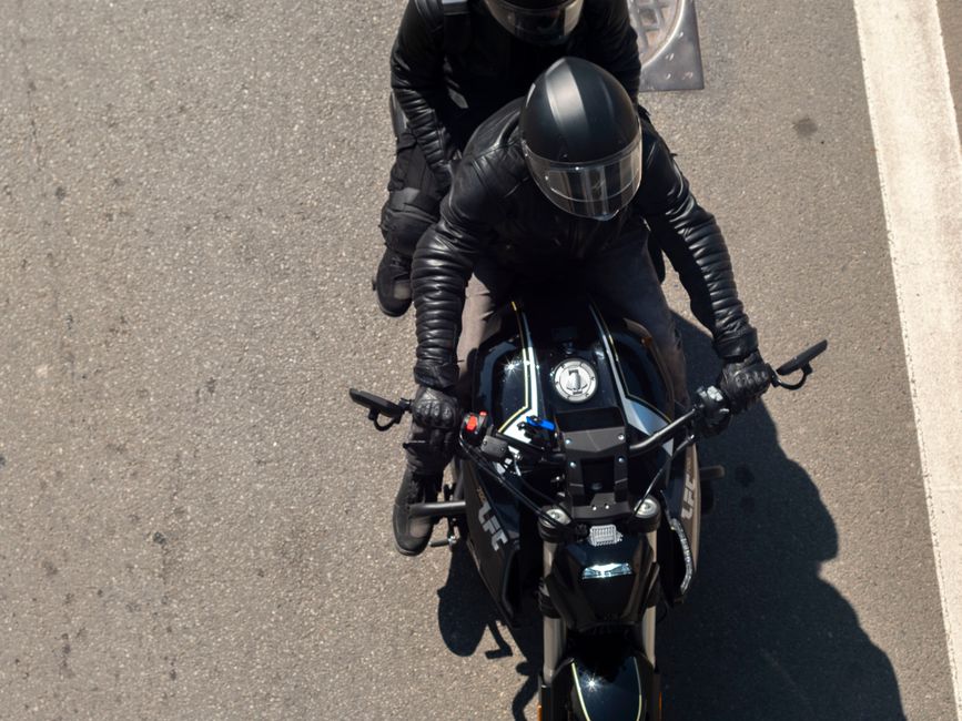 Two motorcyclists in black gear ride on a sunny street in Wrocław, Poland.
