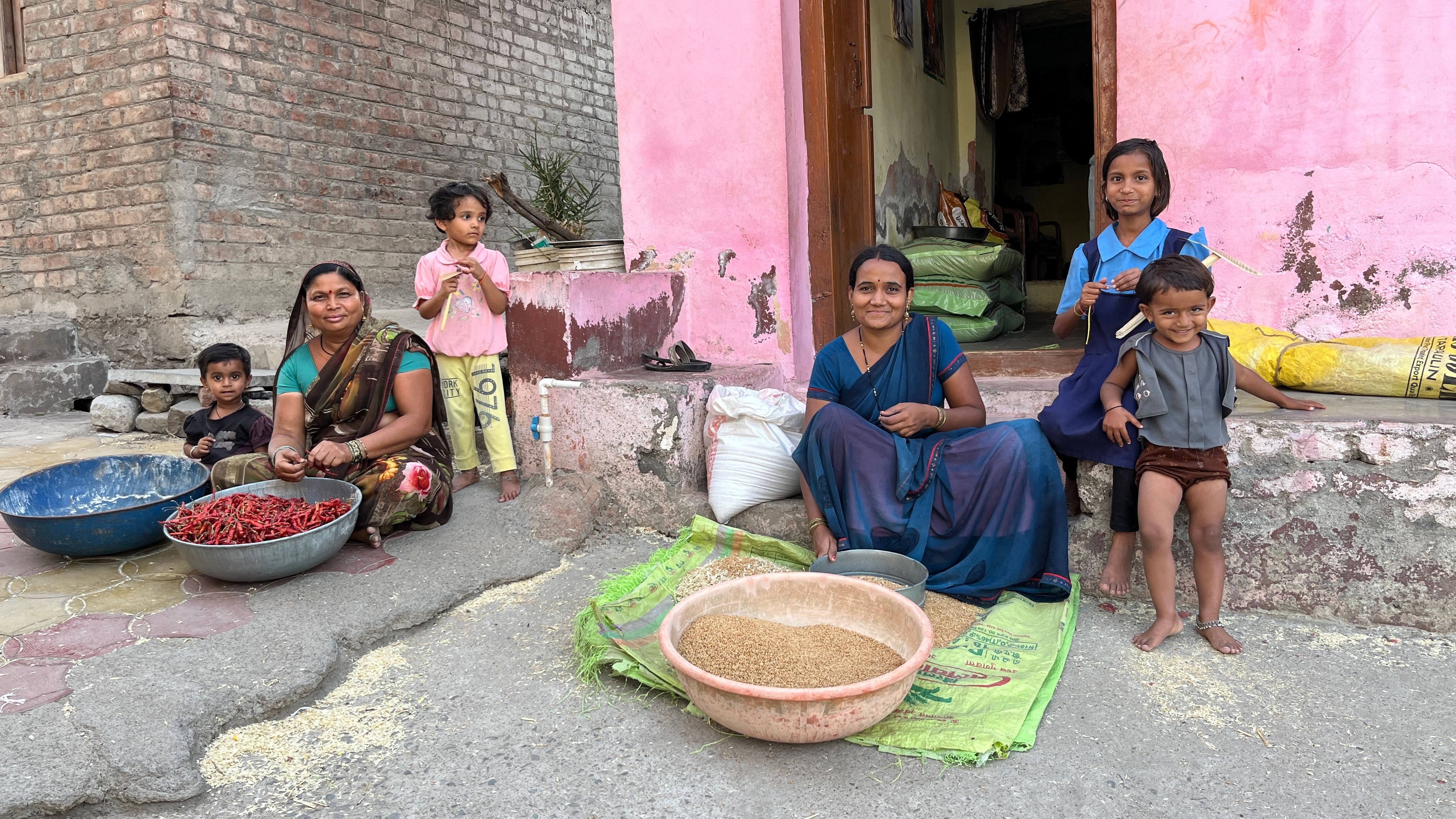 A South Asian family preparing grains and chilies outside their home in India.