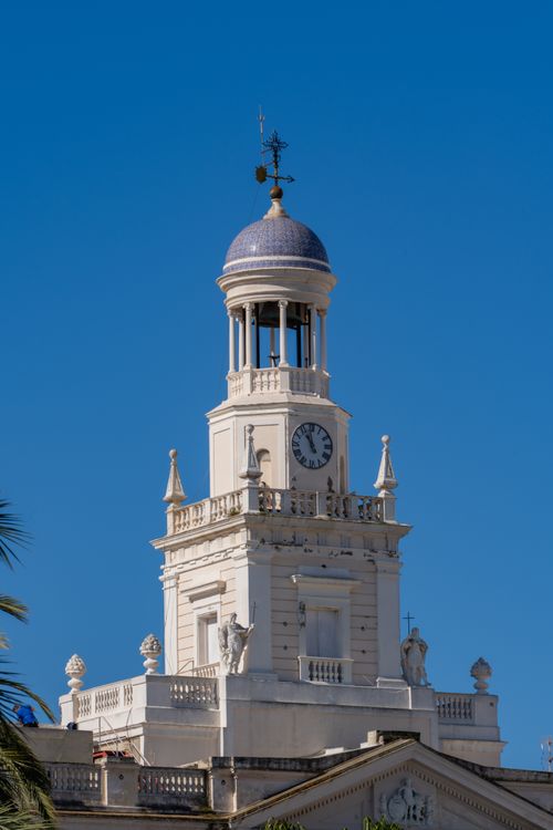 Free A striking view of Cádiz Cathedral's clock tower in Andalucía, Spain, under a vibrant blue sky. Stock Photo