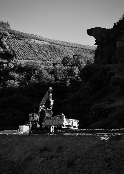 Free Black and white image of an excavator in a quarry with vineyards on the hillside. Stock Photo