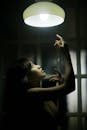 Gorgeous woman raising arms to electric lamp in dark room