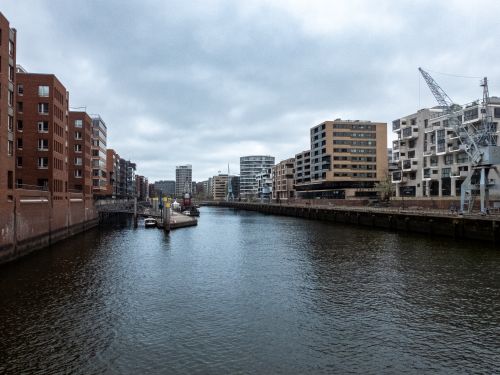 Free Canal flanked by modern buildings under cloudy sky, cityscape view. Stock Photo