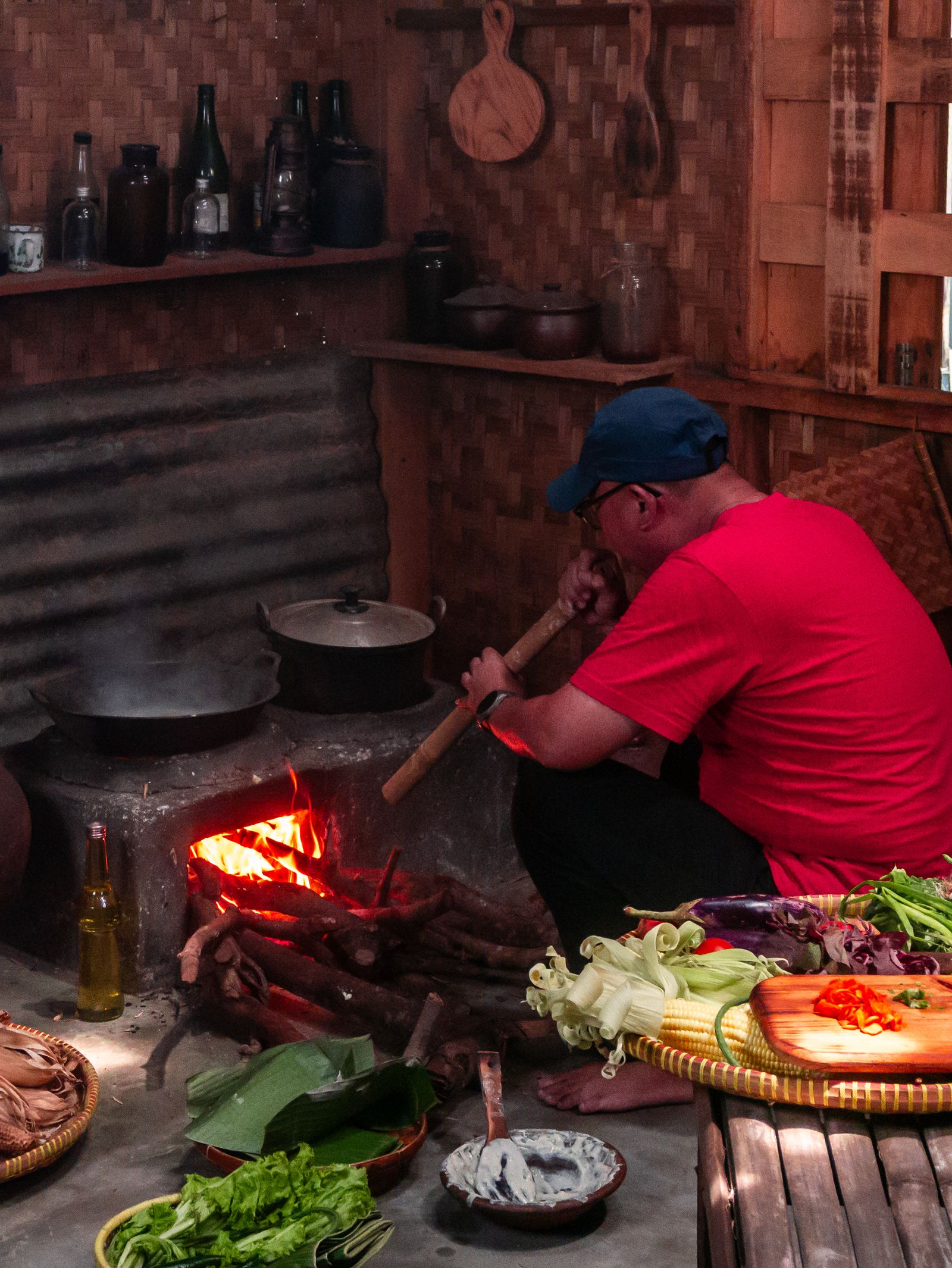 A man in Jakarta prepares a meal using traditional cooking techniques over an open flame in a cozy kitchen.