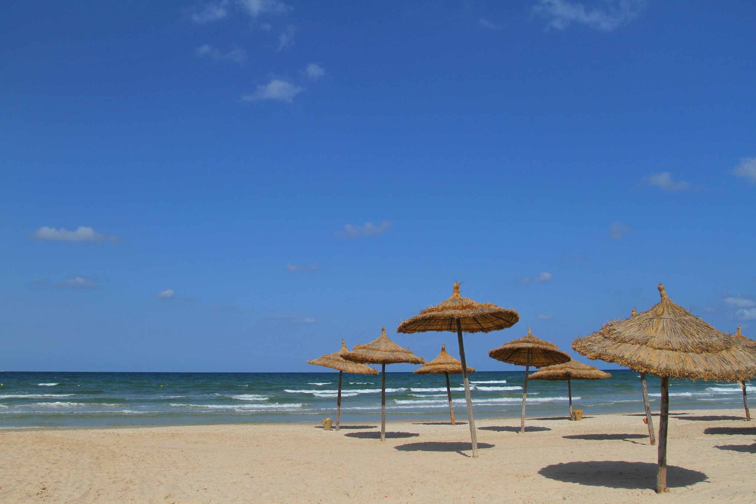 Beautiful sunny day at the beach with straw umbrellas and a clear blue sky.
