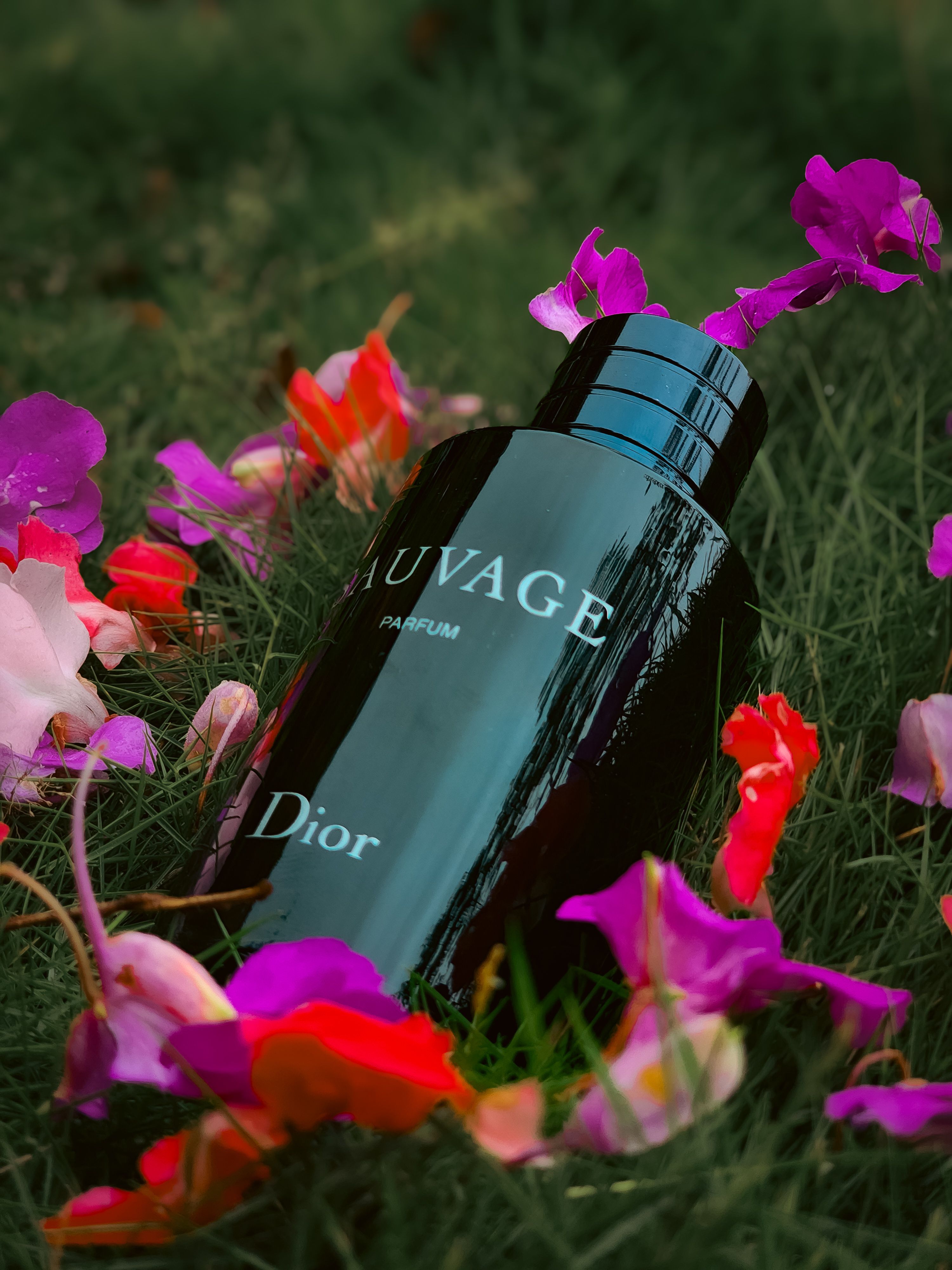 A sleek perfume bottle surrounded by colorful flowers on green grass.